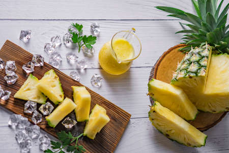 Pineapple cocktail or juice with ice and pineapples on a dark background, Wooden board with fresh sliced pineapple on tableの写真素材