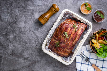 Closeup of pork ribs grilled with BBQ sauce and caramelized in honey with Vegetables and sauces on a drak table, prepared food.の写真素材
