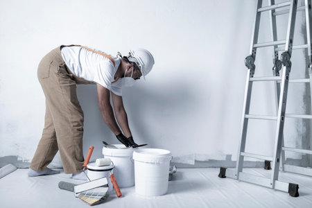 a man paints a white wall with a roller. Repair of the interior. Young male decorator painting a wall in the empty room, concept builder or painter in helmet with paint roller over the empty room.の写真素材
