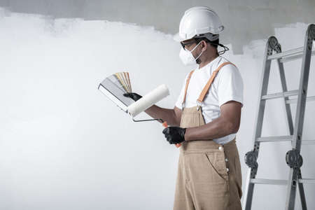 a man paints a white wall with a roller. Repair of the interior. Young male decorator painting a wall in the empty room, concept builder or painter in helmet with paint roller over the empty room.の写真素材