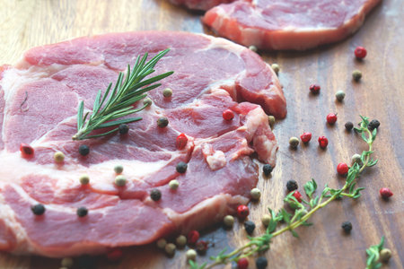 Close up of uncooked raw meat with rosemary and pepper on wooden background