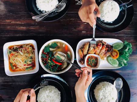 People eating Thai food on a brown wooden table.の写真素材
