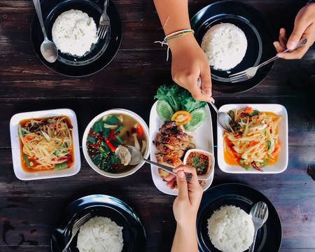 People eating Thai food on a brown wooden table.の写真素材