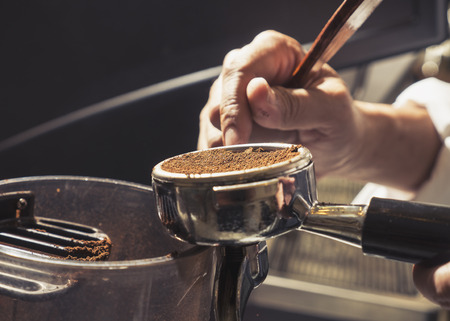Close-up Barista pressing ground coffee into portafilter by tamper to making coffeeの写真素材