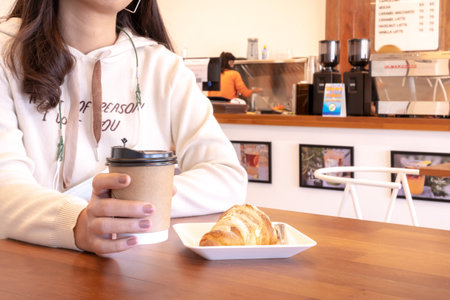 customer holding coffee cup and baked croissant in cafeteriaの写真素材