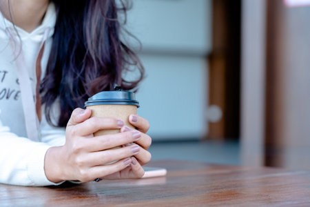 female holding a  paper cup of coffee at cafeteria in the morning.の写真素材