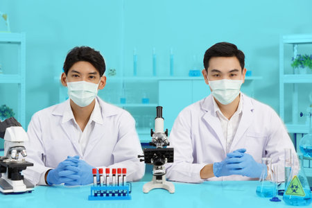 Two Male Scientists wear Face Mask working in Lab while Looking at Camera and Ready to Work and Presentation.  Blue Tone. SARS-CoV-2 , Covid-19 THEME.の写真素材