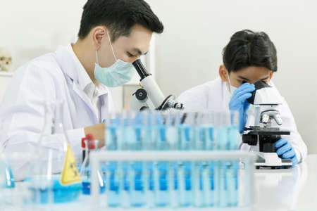 Two Male Scientists with Mask working in Lab while Checking Result of Blood Sample testing on Blue Tubes Foreground. Blue Tone. SARS-CoV-2 , Covid-19 THEME.の写真素材