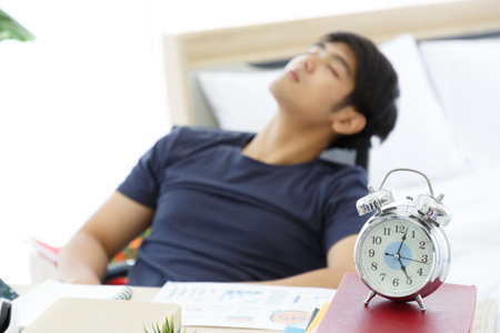 Clock on Table in front of Tired Asian man napping at a office after a hard workday, working on desk, tried, Work From Home.の写真素材
