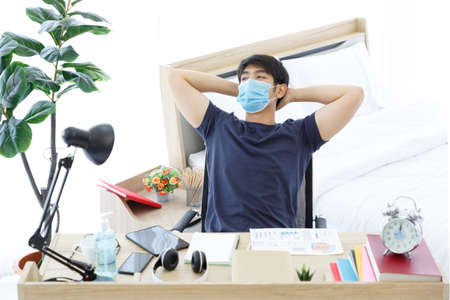 Tired asian man wearing Mask. using tablet sitting on desk While Stretching Moment. COPY SPACE. Trading Online. WORK FROM HOME WFH Concept.の写真素材