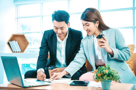 Business couple sitting together with laptop and checking work on table near the window background.の写真素材
