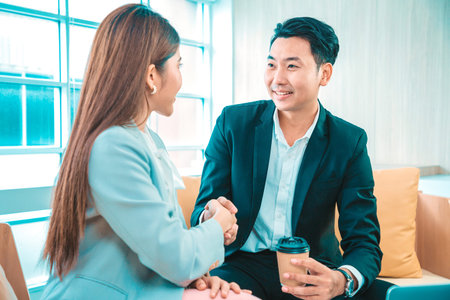 Business people shaking hands. Young modern man and woman in smart casual wear shaking hands while working in the office.の写真素材