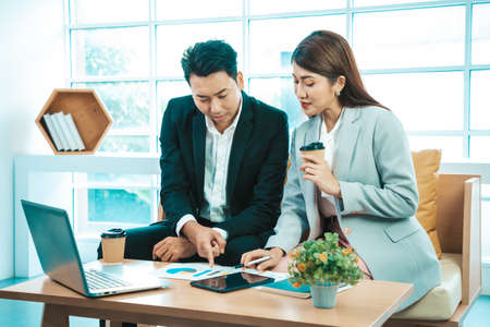 Business couple sitting together with laptop and checking work on tablet near the window background.の写真素材