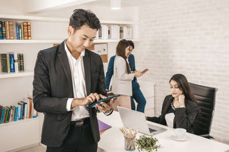 Portrait of a handsome CEO smiling, Portrait of a positive looking young business professional standing with using tablet with coworkers talking in the background.の写真素材