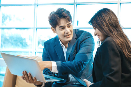 Businessman and businesswoman sitting together with laptop and checking work on sofa in the office.