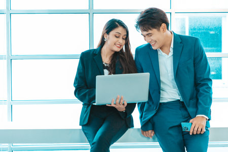 Businessman and businesswoman sitting together with laptop and checking work on window background.の写真素材