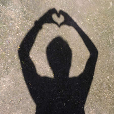 Man's shadow forming a heart shape with his handsの写真素材
