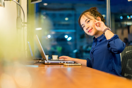 Young woman working at a laptop in the office at night time. Business woman - office worker. Bored young woman sitting at her desk in front of laptop. She is working overtime. Selective focus.の写真素材