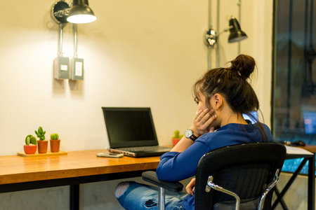 Young woman working at a laptop in the office at night time. Business woman - office worker. Bored...