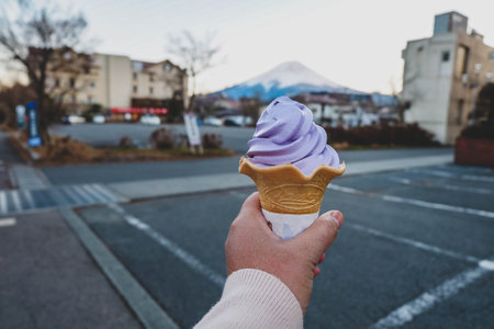 Ice cream cone in a hand with village and mountain background.の写真素材