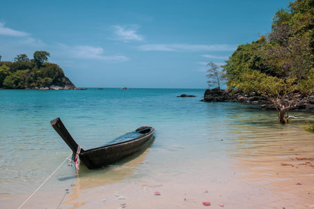 Scenery of paradise beach with small island and long tail boat parked on emerald blue seaの写真素材