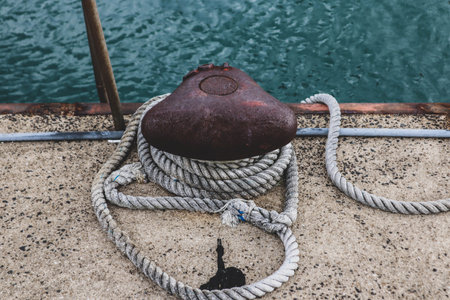 Weathered rope coiled around a rusty bollard on a seaside pier â a quiet moment by the harbor, where time and tide leave their mark.の写真素材