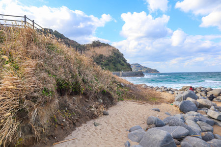 Rocky Coastal Landscape with Grassy Hills and Ocean Waves under Cloudy Skyの写真素材