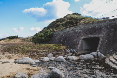 A natural stream flowing past a weathered sea wall.の写真素材