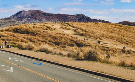 Scenic view of the vast Aso caldera with a road and walking path in the foreground and a distant volcanic peak.の写真素材
