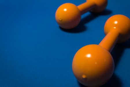 Closeup of an orange dumbbell, with another dumbbell by its side, against a blue background.の写真素材