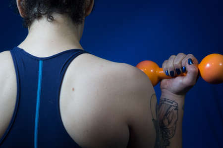 Shot of the back of a woman holding up an orange dumbbell by the side of her bodyの写真素材
