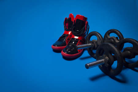 Shot of two iron dumbbells by two red training boots, against a blue background.の写真素材