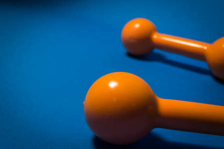 Closeup of an orange dumbbell, with another dumbbell in the back of the picture.の写真素材