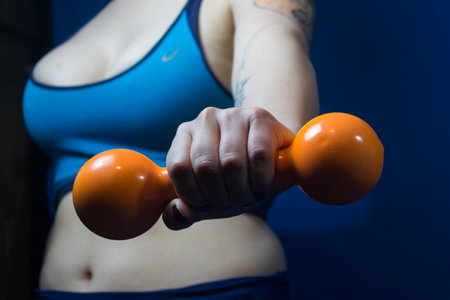Closeup of an orange dumbbell held by a woman out of focusの写真素材
