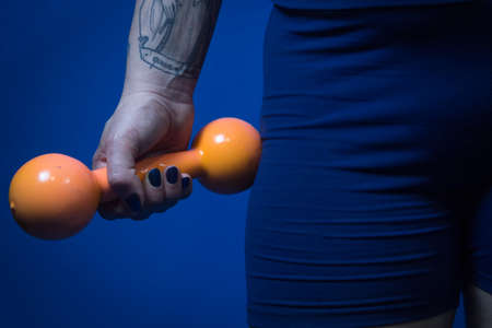 Woman holding an orange dumbbell by the side of her bodyの写真素材