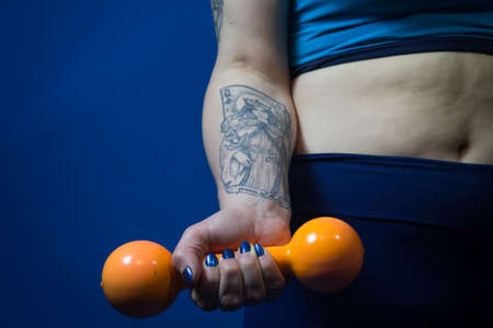 Woman holding an orange dumbbell by the side of her bodyの写真素材
