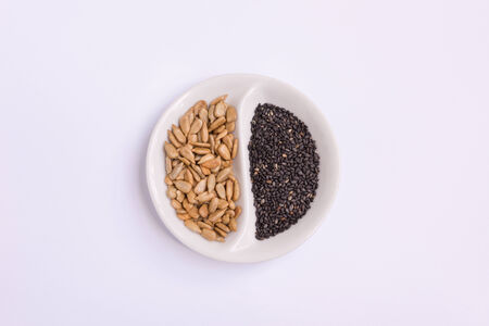 close up look of sunflower kernel and black sesame seed in a white small devided dishの写真素材
