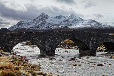 Old stone bridge over a wide stream in mountainsの写真素材