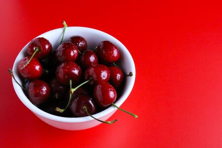 Fresh fruit cherries in a bowl with a red background.の写真素材