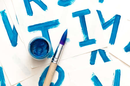 Alphabet drawing. Process of creating watercolor font. Blue gouache in the jar and brush on background with blue colored letters.の写真素材