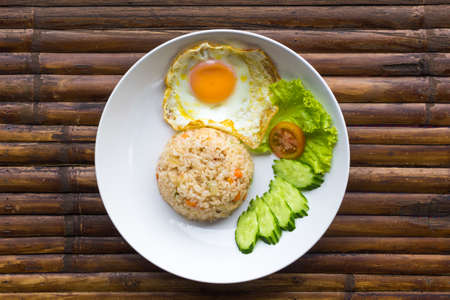 Scrambled egg, rice and fresh vegetables on white plate on brown bamboo table. Thailand breakfast. Top view.の写真素材