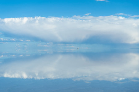 Car at Uyuni Salt Flats. Altiplano, Bolivia. Rainy Season. Tunupa Volcano. Clouds Reflection on Water in Lake Surfaceの写真素材