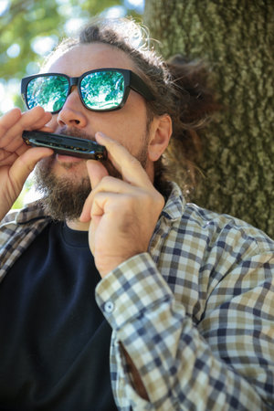 Man with Dreadlocks Ponytail Wearing Sunglasses Playing Music with Harmonica, Mouth Organ. Standing...