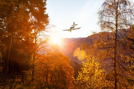 airplane flying in autumn landscape at sunsetの写真素材