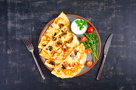 Delicious pancakes with mushrooms, ham and cheese, arugula, tomatoes and sour cream on a wooden backgroundの写真素材
