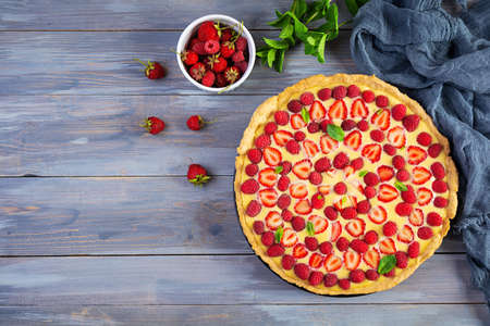 Delicious homemade tart with strawberries and raspberries garnished mint leaves on wooden...