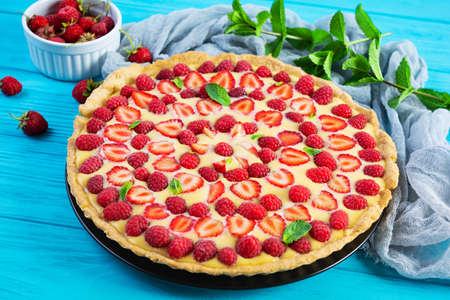 Delicious homemade tart with strawberries and raspberries garnished mint leaves on wooden backgroundの写真素材