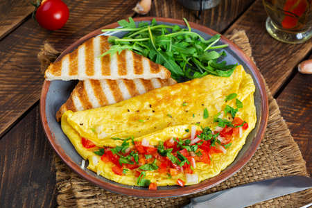 Fried omelette with tomatoes, onion and herbs. Delicious breakfast with eggs and toastsの写真素材