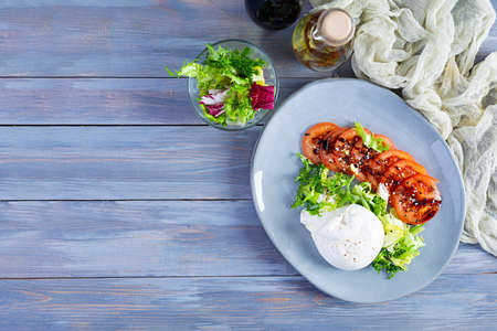 Fresh salad with burrata, lettuce and tomatoes. Delicious Italian cheese made from mozzarella and...