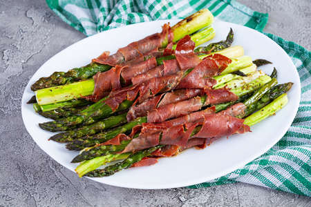 Baked asparagus with bacon and herbs on wooden background